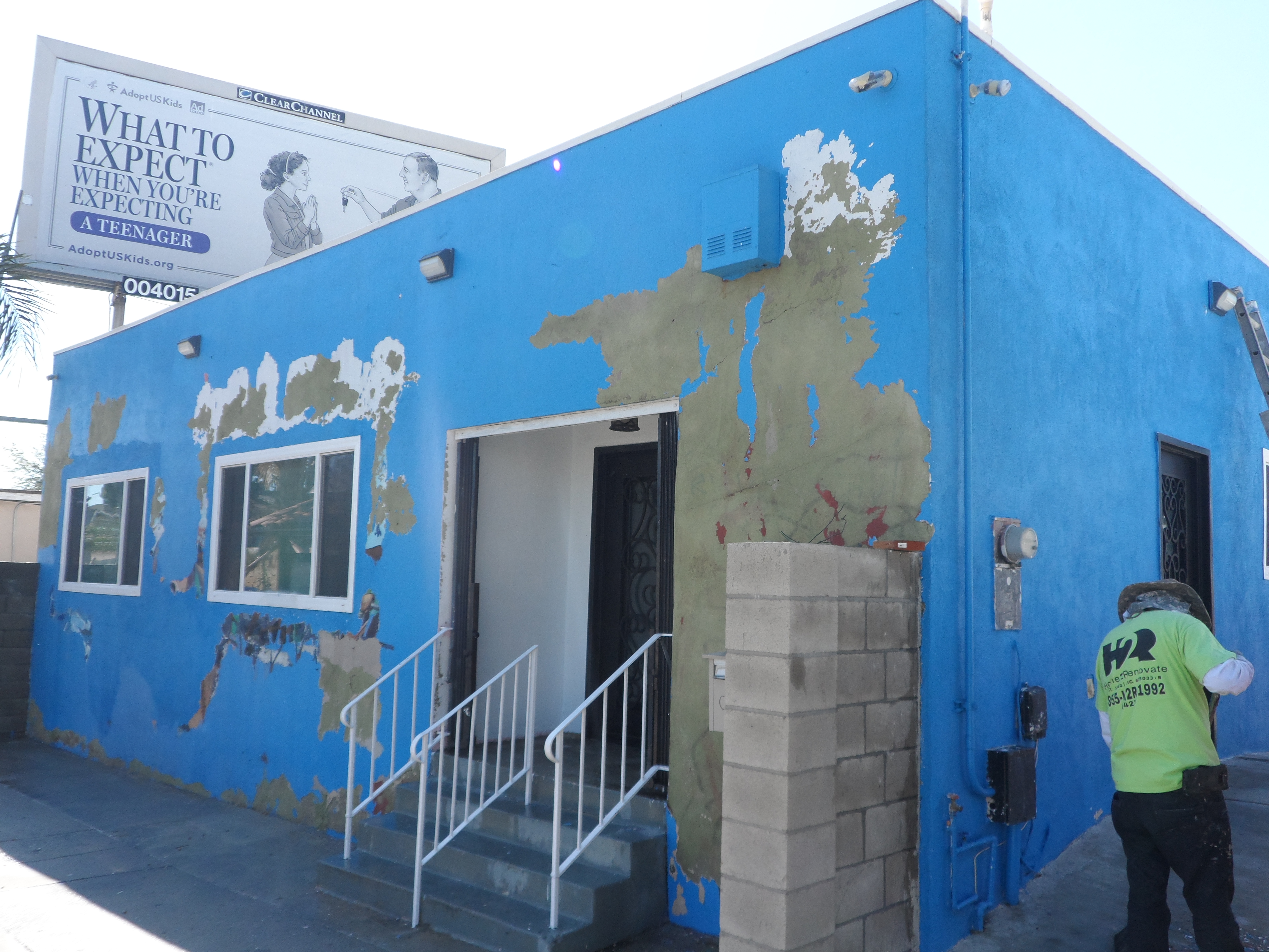 A blue building with peeling paint and steps leading to it.