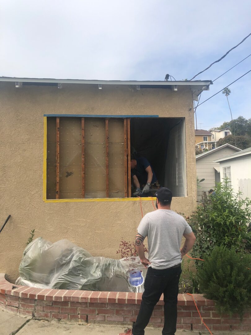 A man standing in front of a window with a construction worker looking out.