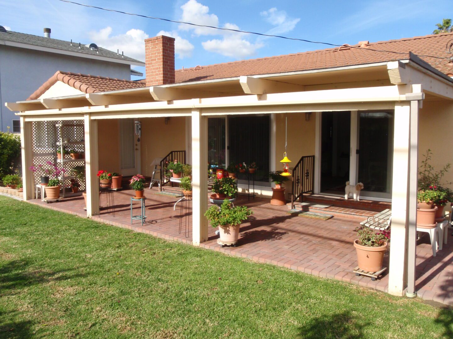 A patio with chairs and potted plants on the grass.