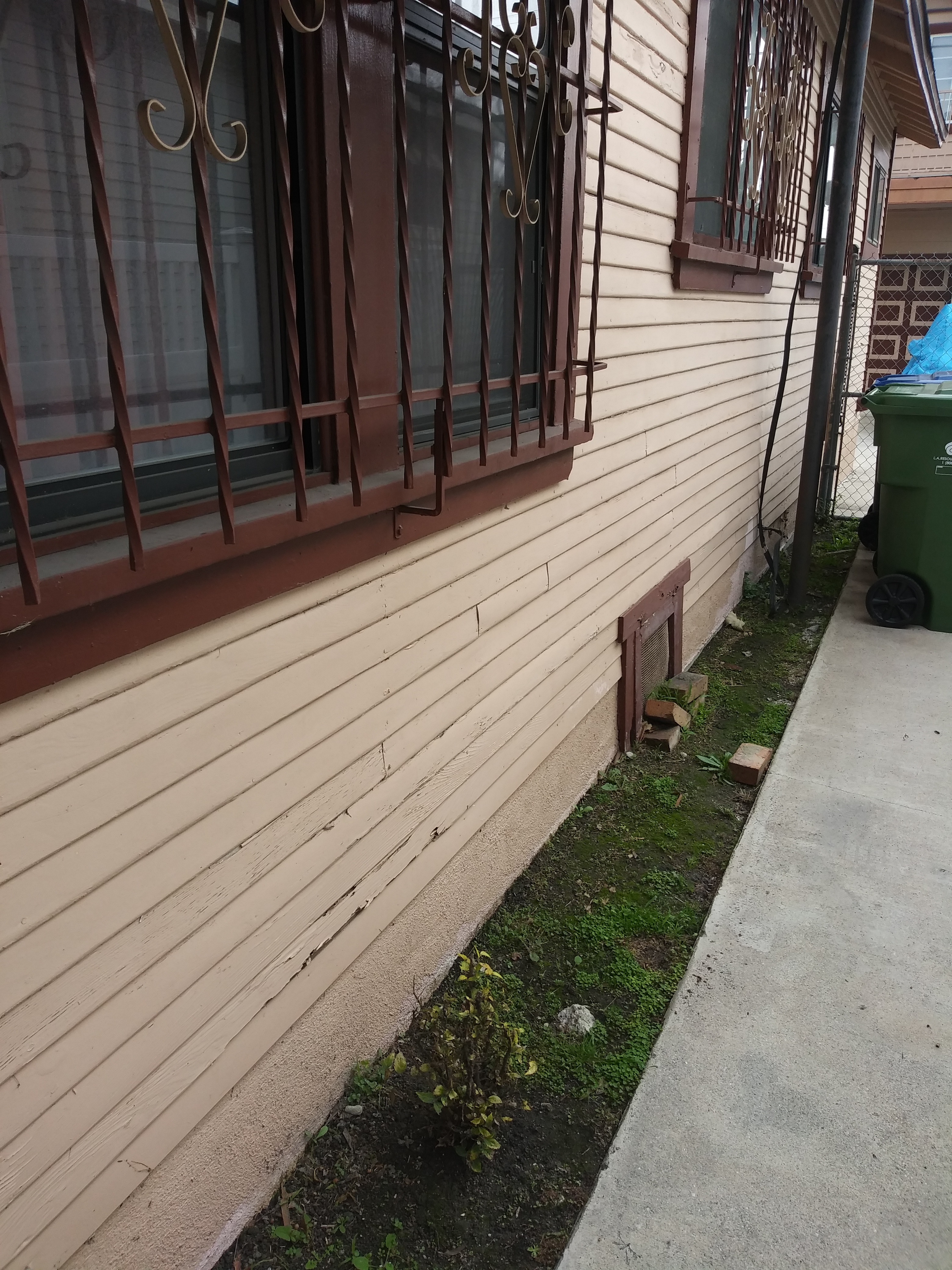 A green garbage can sitting on the side of a building.