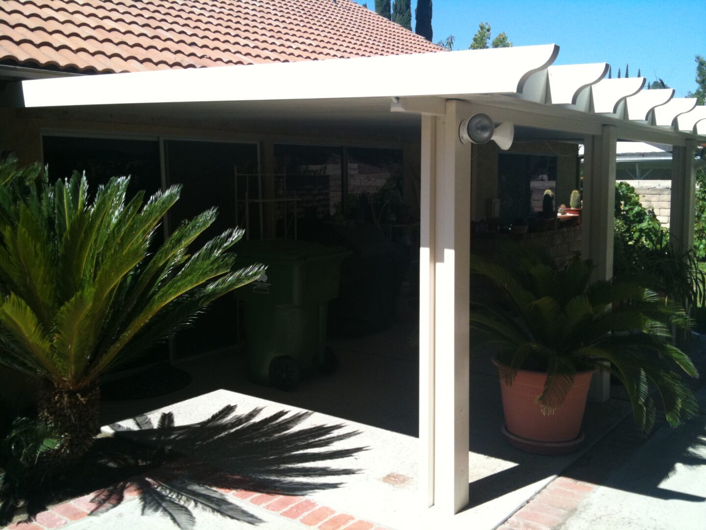 A white patio cover with potted plants in front of it.