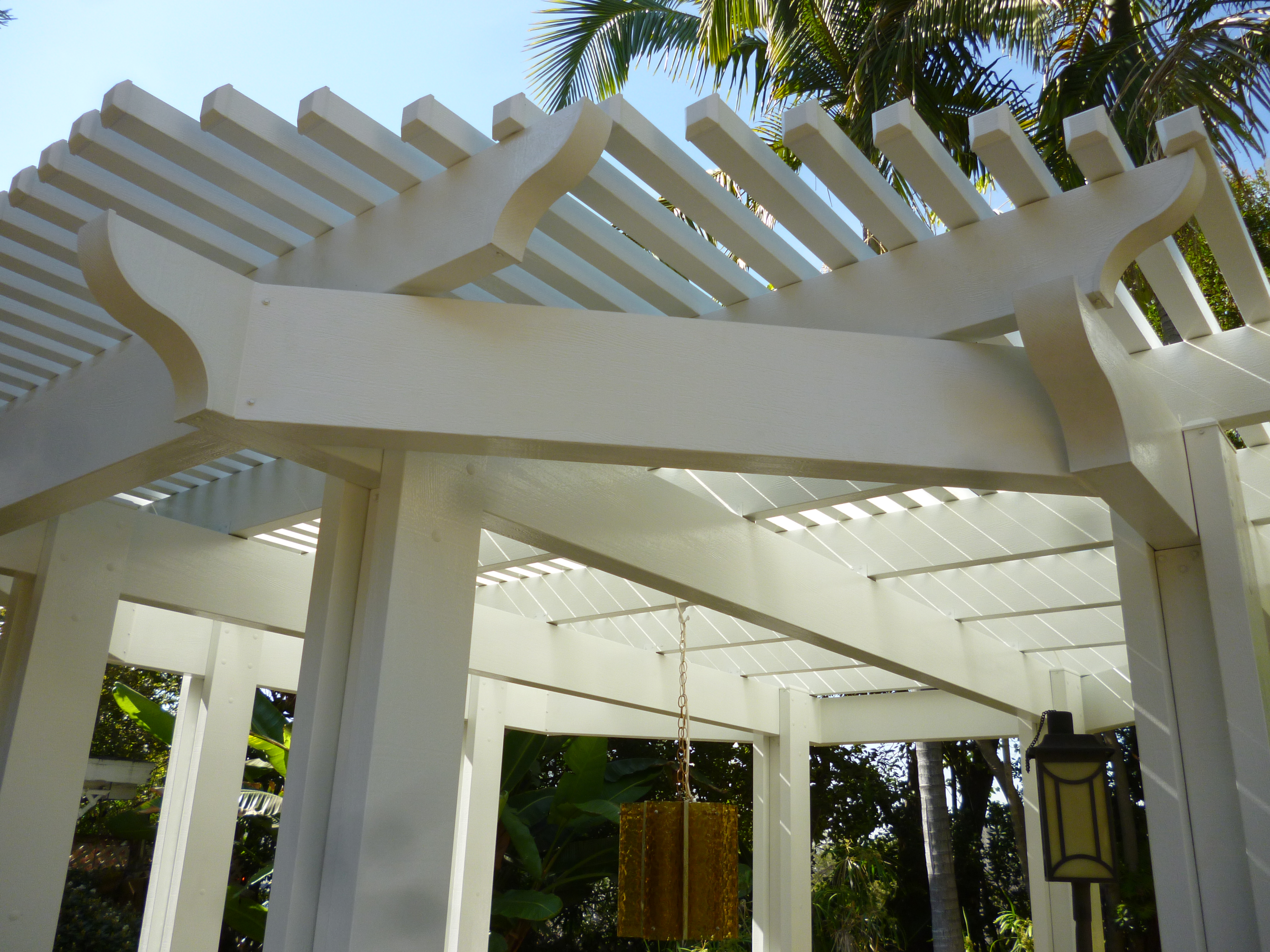 A white pergola with palm trees in the background.