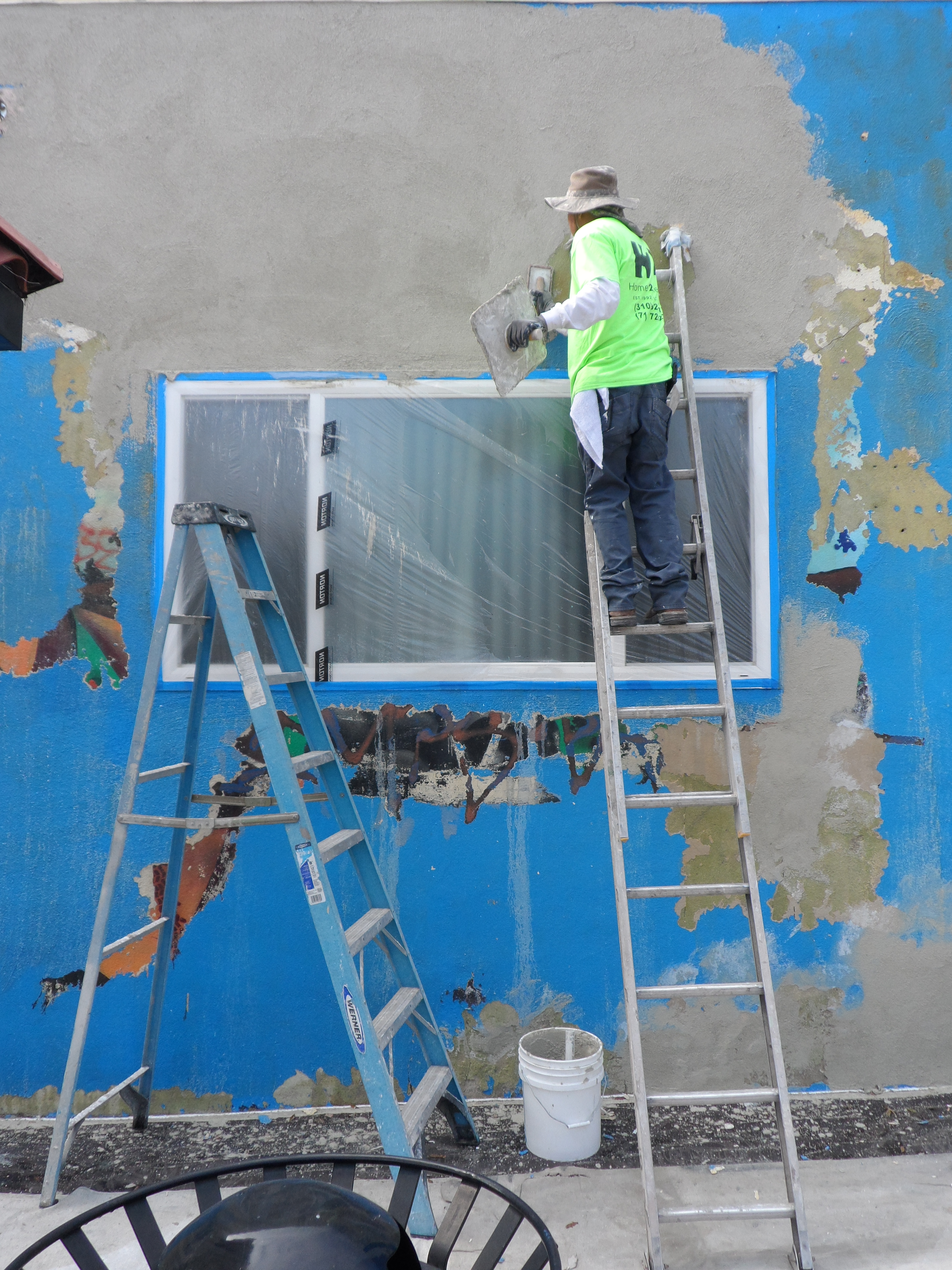 A man on a ladder painting the side of a building.