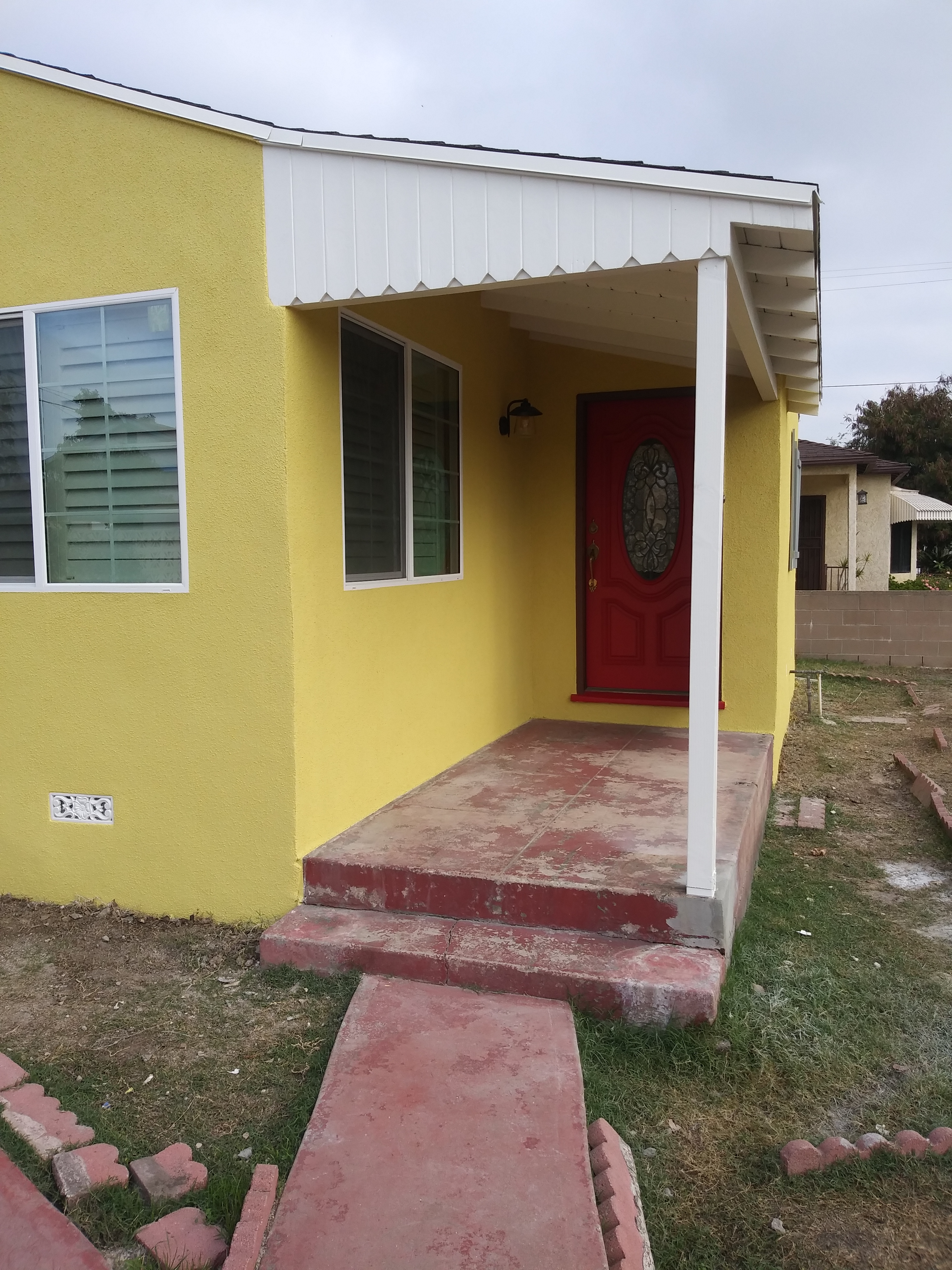 A yellow house with red door and white porch.