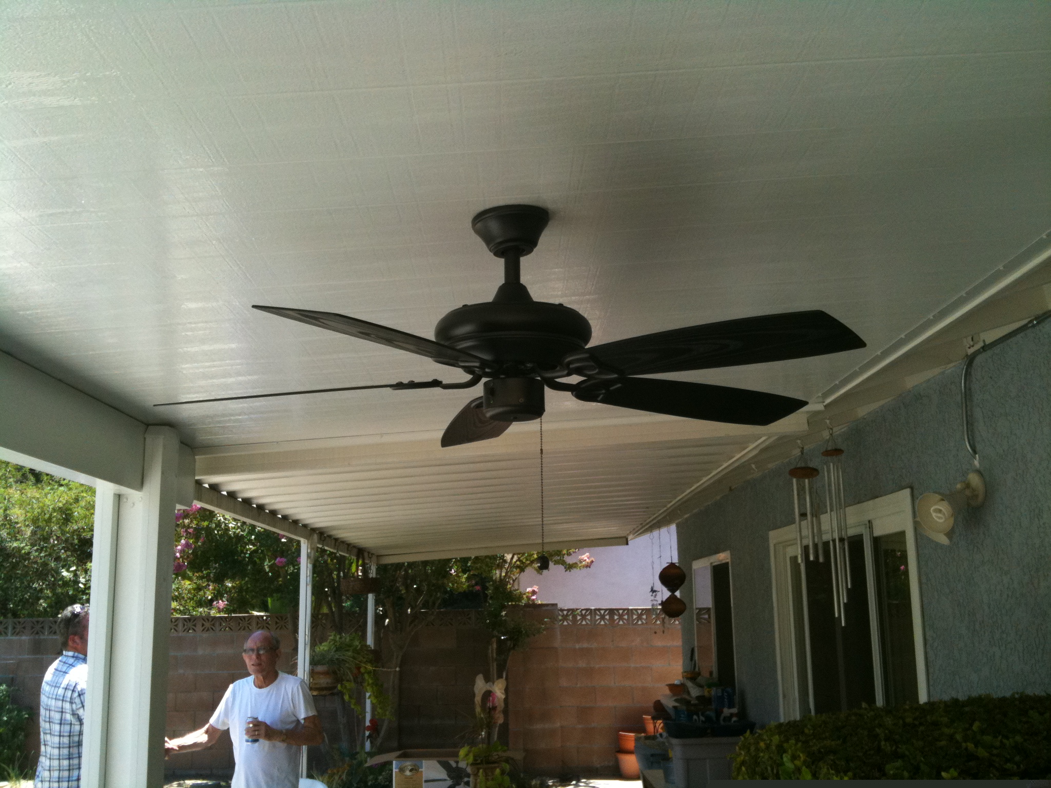 A man standing in front of an outdoor ceiling fan.