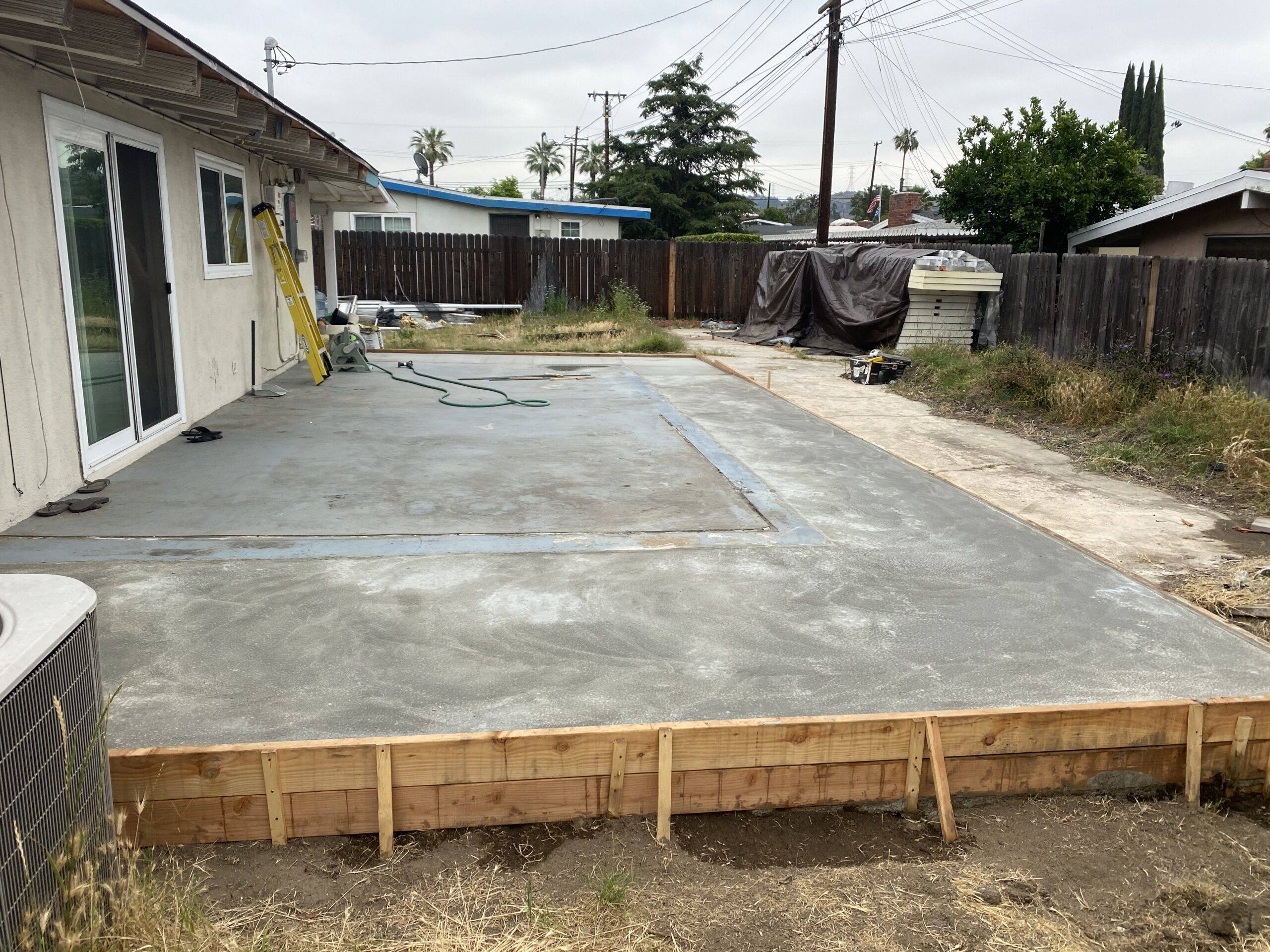 A concrete slab being installed in the backyard of a house.